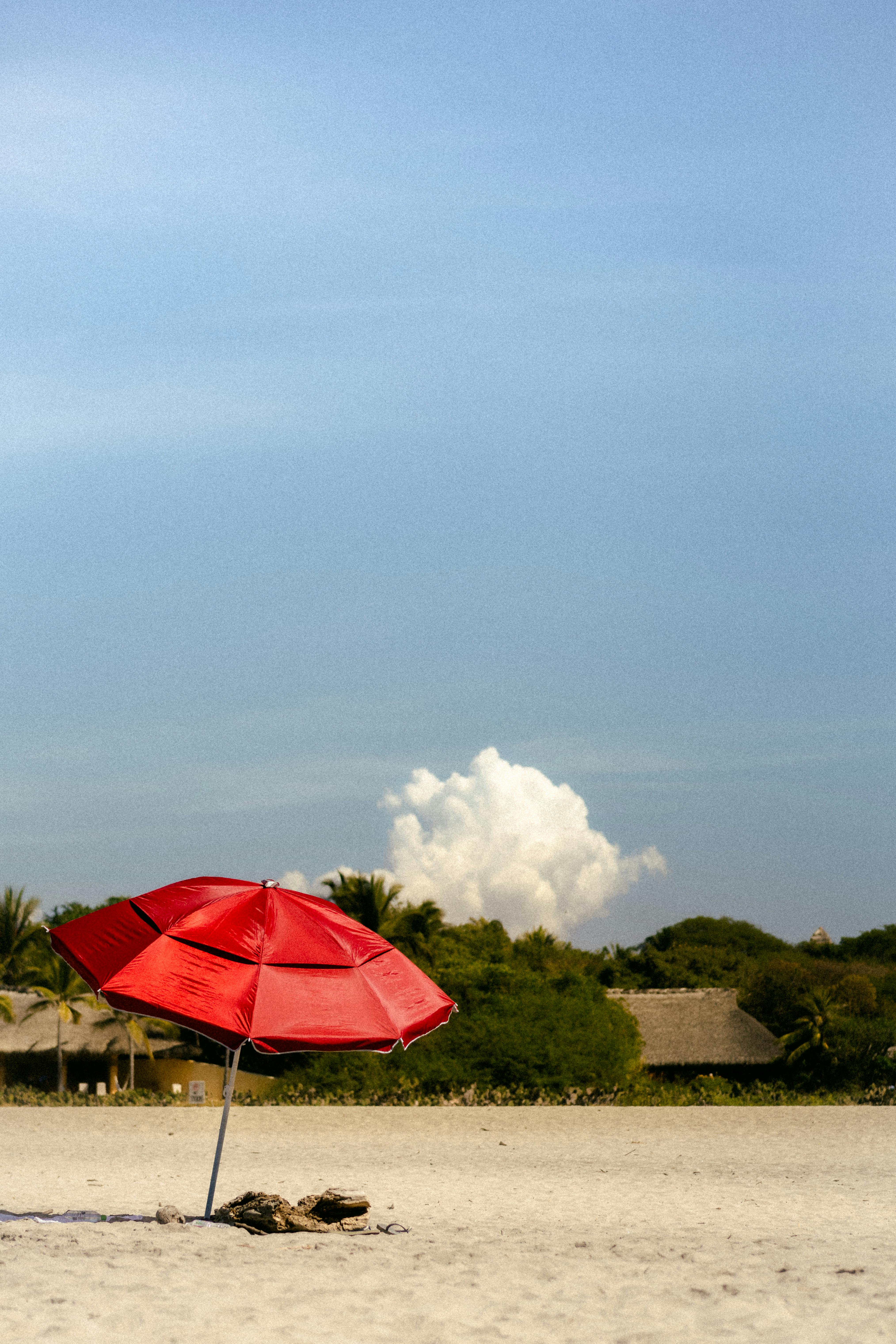 A tranquil beach scene in Oaxaca, featuring a vibrant red umbrella against a tropical backdrop.