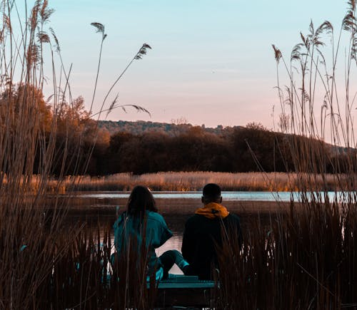 Man and Woman Sitting Near Body of Water during Golden Hour