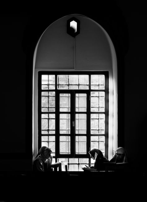 Black and white photo of nuns reading by a large window, creating a serene and contemplative scene.