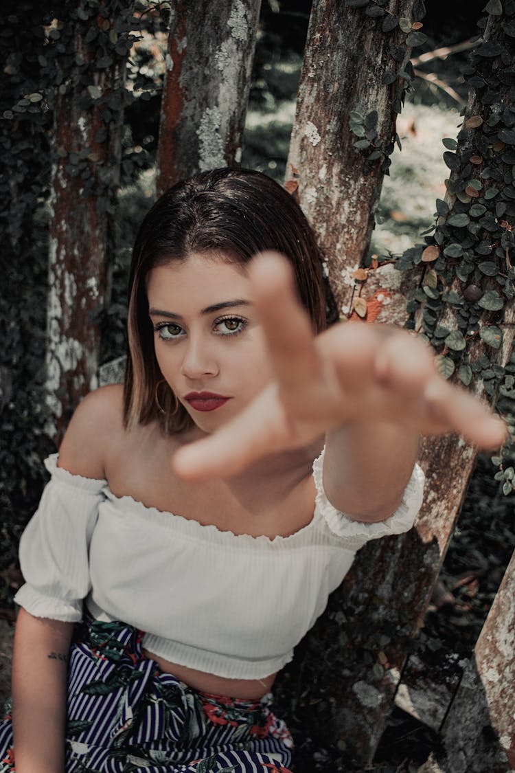 Photo Of Woman In White Off-shoulder Top Sitting By Tree Reaching Out Her Hand