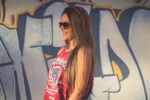 Foto De Vista Lateral De Mujer Sonriente En Camiseta Roja Y Gafas De Sol Cerca De La Pared De Graffiti