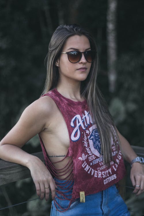 Photo of Woman in Red Tank Top and Sunglasses Leaning on Wooden Railing