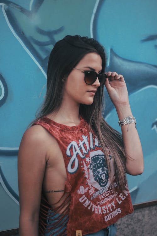 Free Side View Photo of Woman in Red Tank Top and Sunglasses Standing Near Graffiti Wall Stock Photo