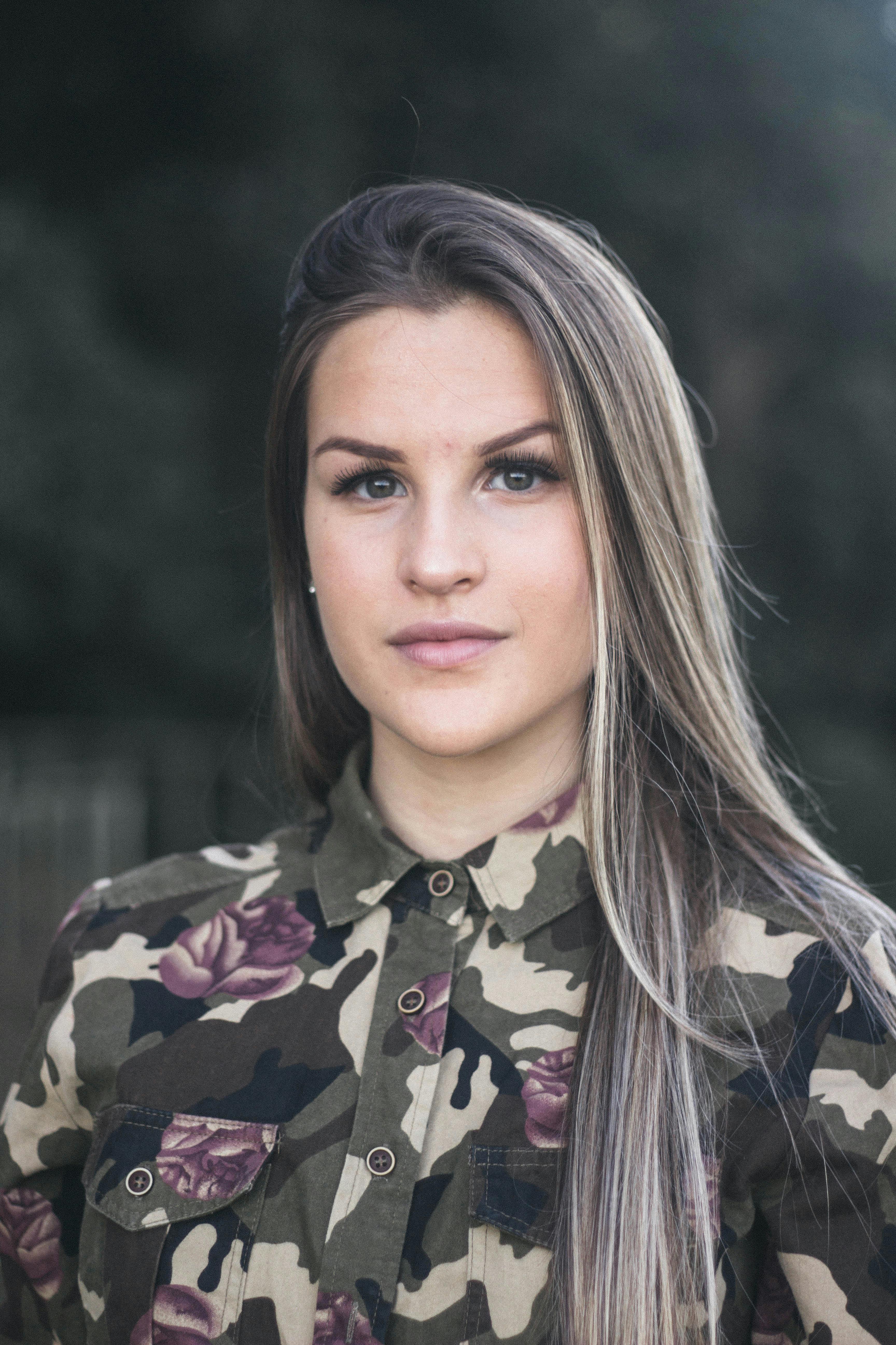 一位穿着迷彩衬衫、留着长发的女子在户外的特写肖像