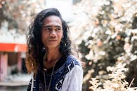 一个留着长发、戴着项链的有思想的男人，在城市户外环境中移开了目光