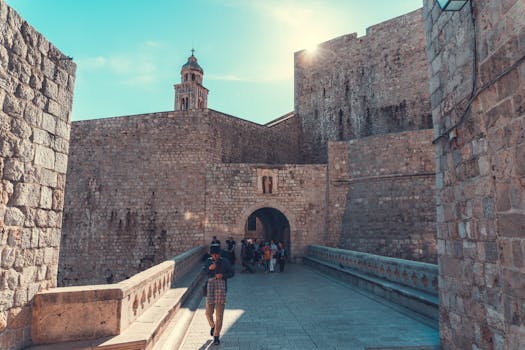 一座中世纪堡垒的石墙在阳光下显得格外明亮，桥上还有游客