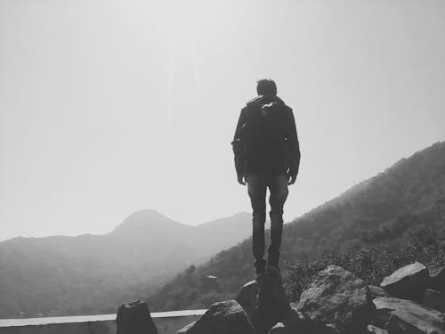 Grayscale Photo of Man Standing on a Cliff