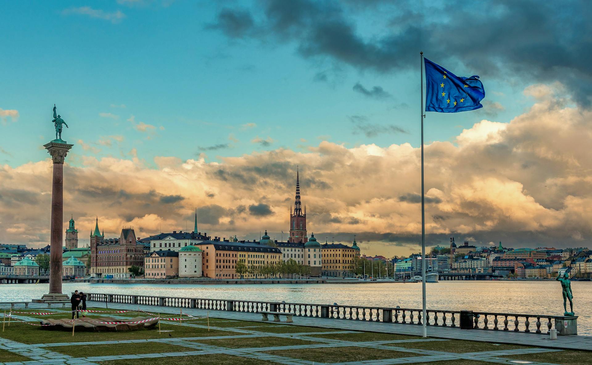 Beautiful Stockholm waterfront view with iconic buildings and EU flag under a dramatic sunset sky.