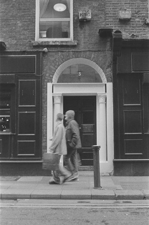 Two people walking down the street in front of a building