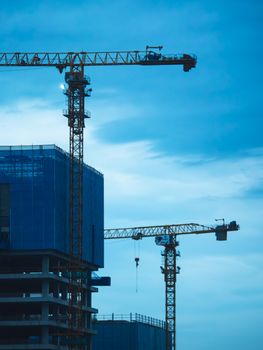 Tall cranes at a construction site against a twilight sky in the city, capturing urban development.
