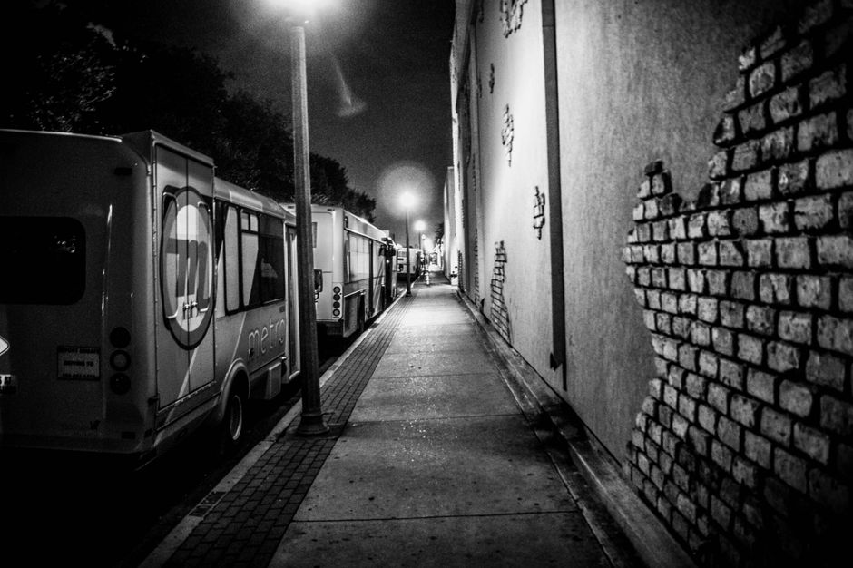 A moody black and white street scene with parked buses at night.