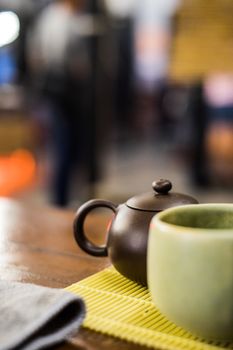 A traditional teacup and teapot on a wooden table with blurred background, evoking a cozy indoor ambiance.
