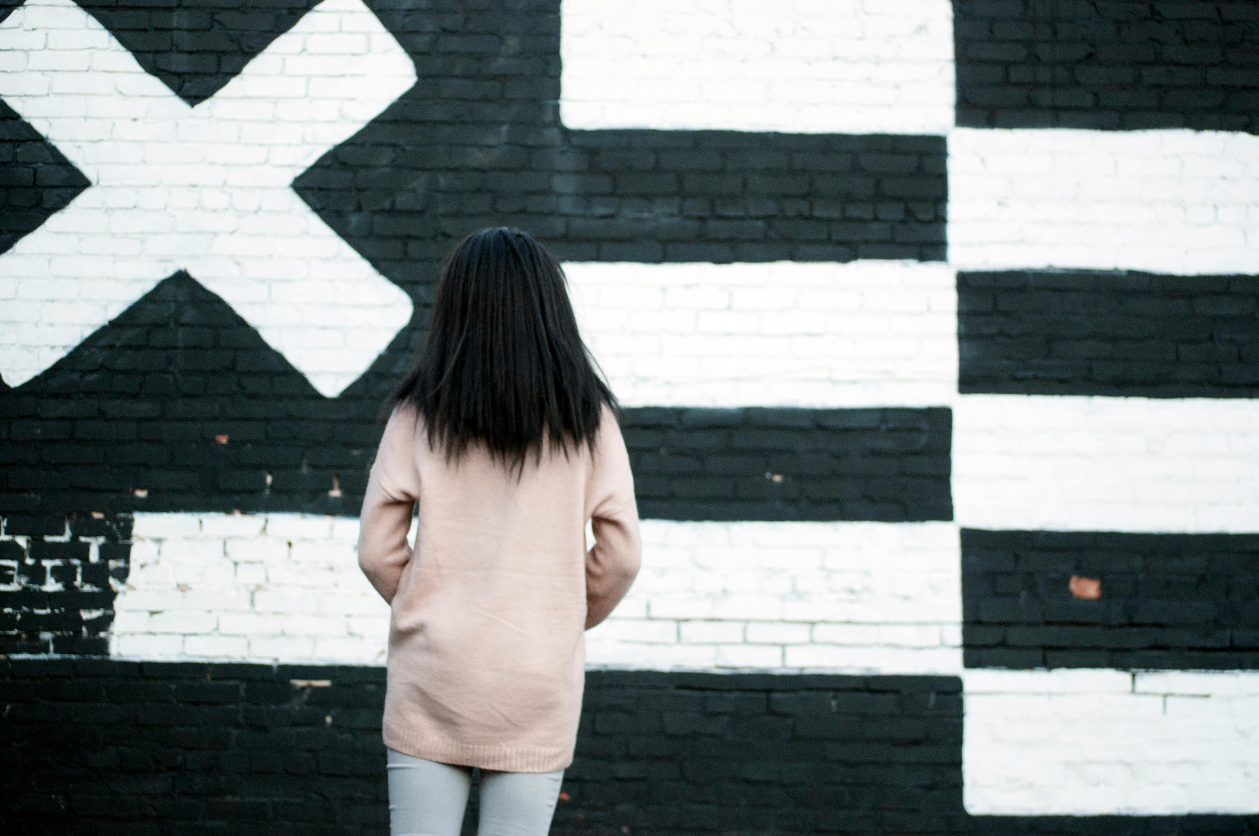 Brunette woman stands alone against a striking black and white mural wall.
