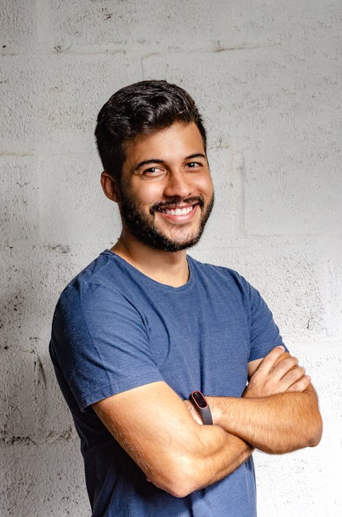 Portrait Photo of Smiling Man with His Arms Crossed Standing In Front of White Wall