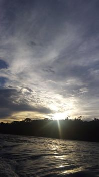 Captivating view of the sun setting over the ocean with dramatic clouds and silhouetted trees.