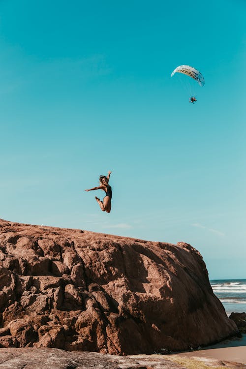 Woman Jumping on Brown Rock Formation