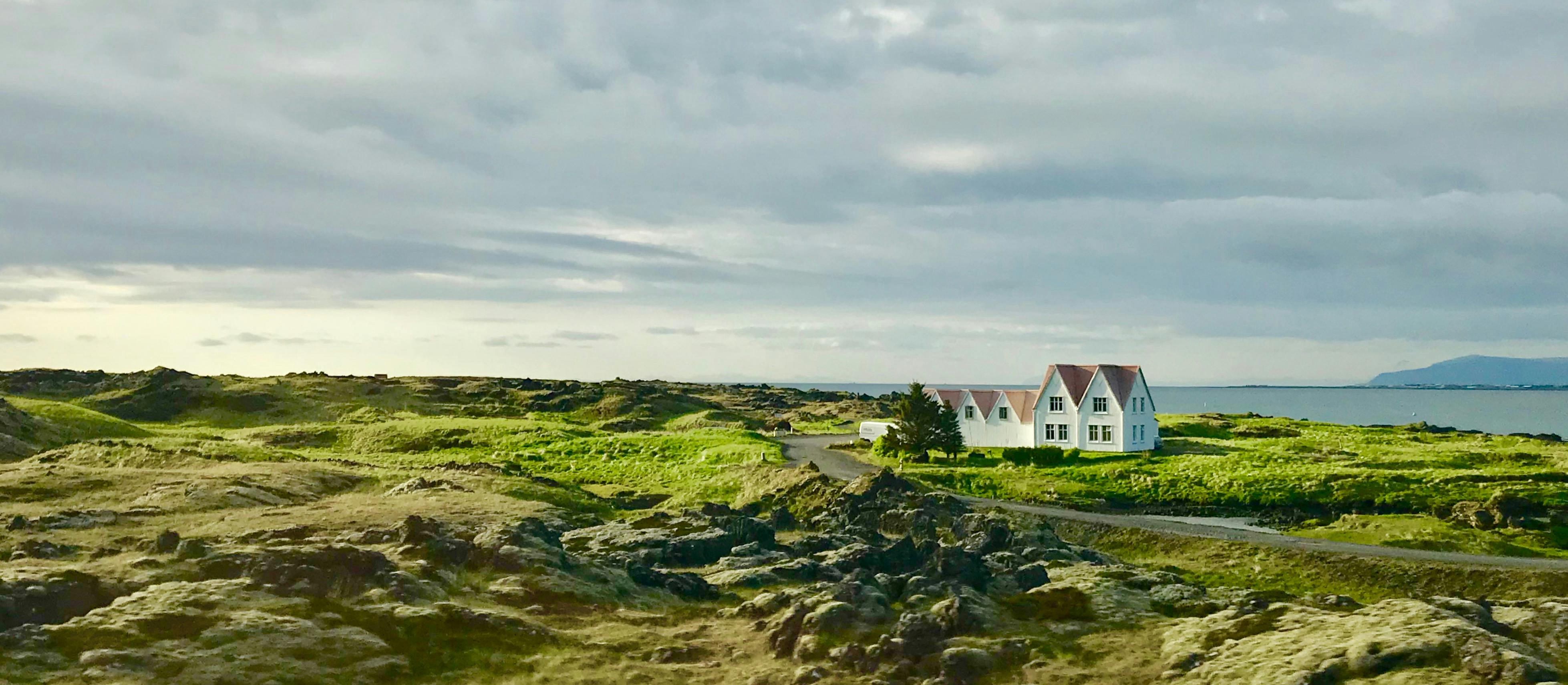 在广阔的天空下，郁郁葱葱的绿色植物和岩石景观环绕着美丽的沿海房屋
