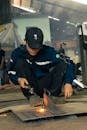 Man in Cap Squatting and Welding