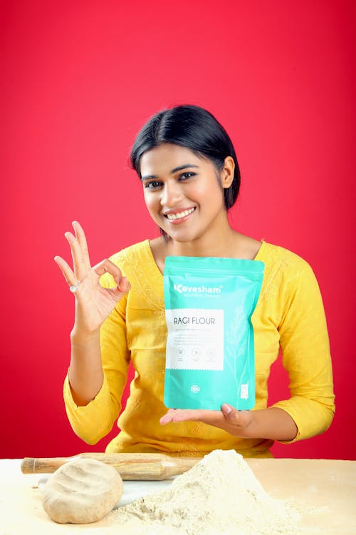 A woman holding a bag of flour and giving the ok sign