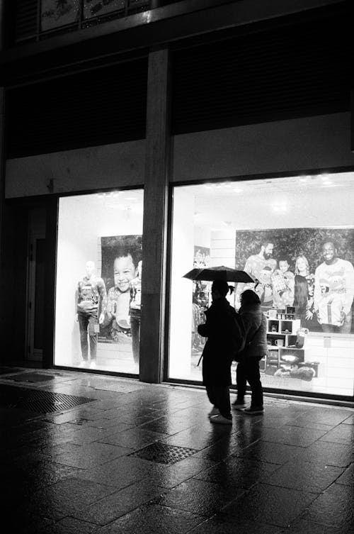 Two people are standing in front of a store with an umbrella