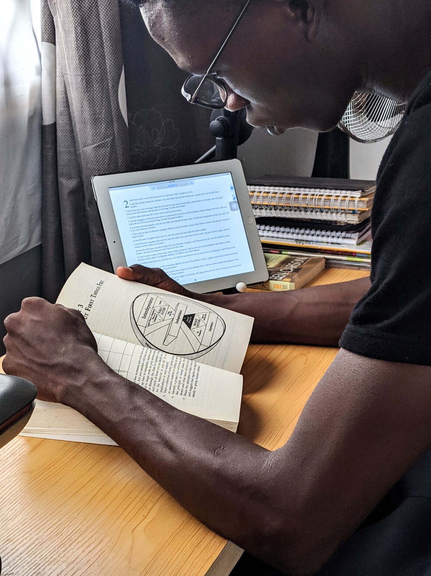 A person studying at a desk with a book and tablet