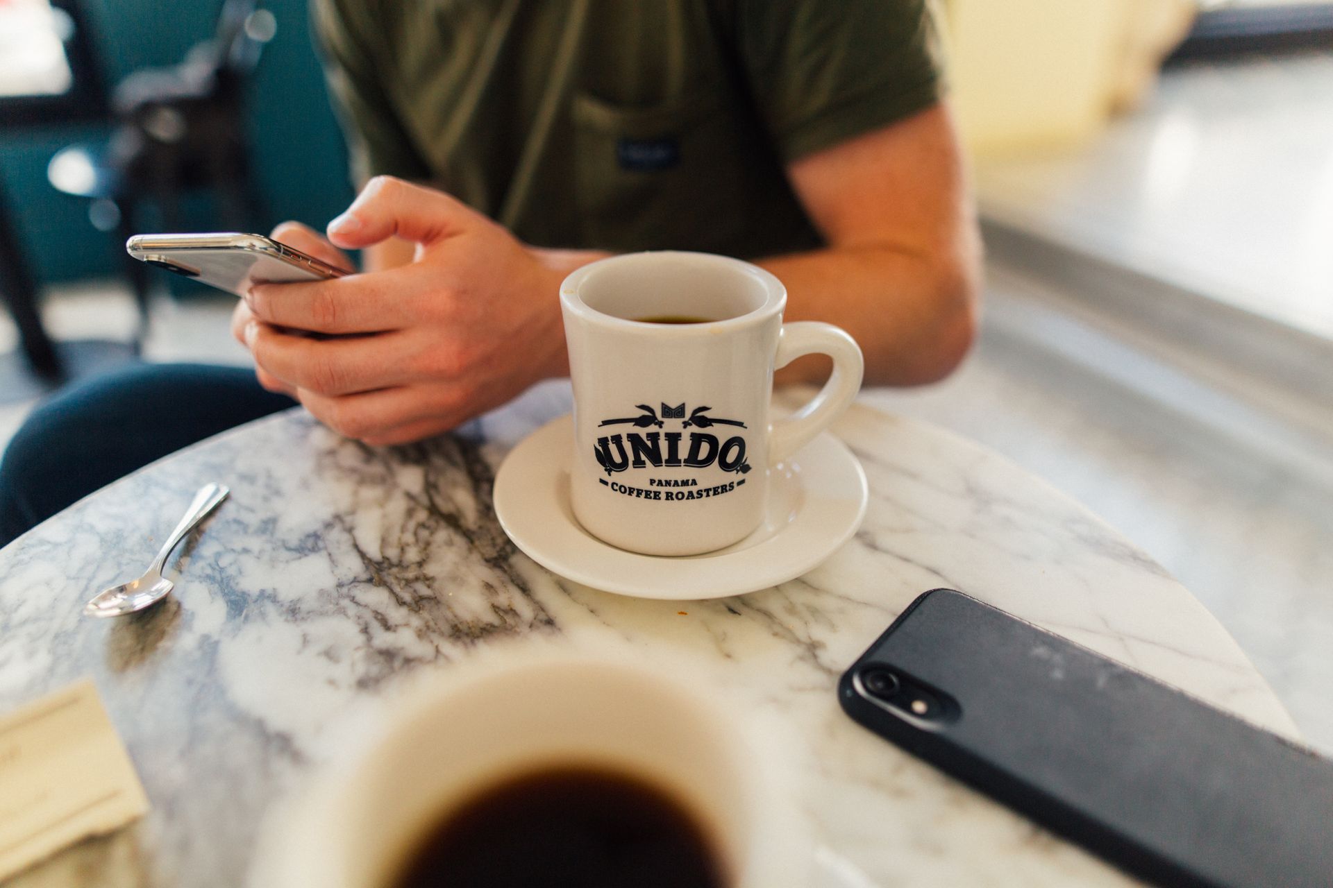 A person using a smartphone while enjoying coffee in a Panama café. Marble table adds elegance.