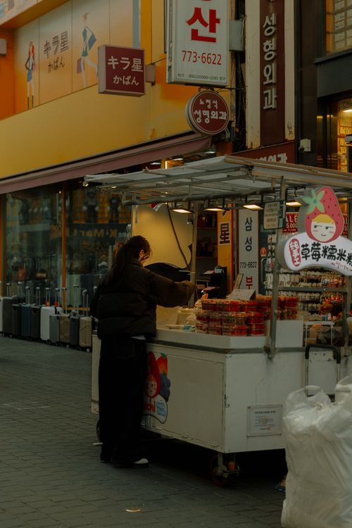 Free Person buying street food in an urban Asian market setting with colorful signage. Stock Photo