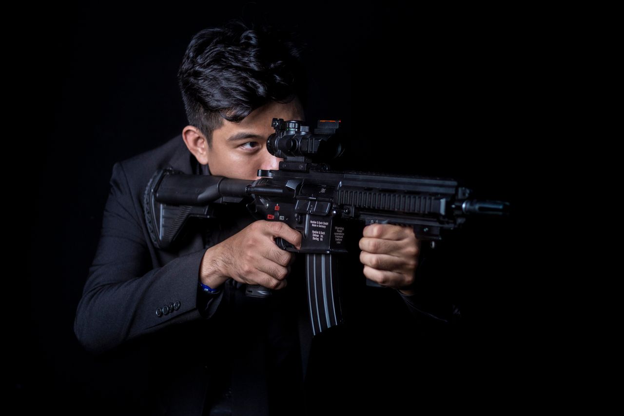 portrait of a man aiming a rifle with a focused expression against a b