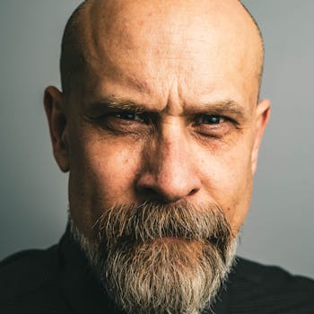 Close-up portrait of a serious bald man with a beard, conveying intensity and thoughtfulness.