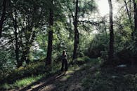 一名妇女独自走在阳光明媚的林间小路上，四周绿树环绕