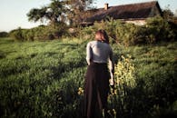 一名妇女穿过郁郁葱葱的绿地，走向晴朗天空下的一栋老房子