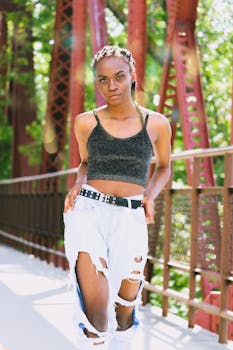 一位穿着破洞牛仔裤和露脐上衣的时尚女性，在阳光明媚的户外摆着姿势