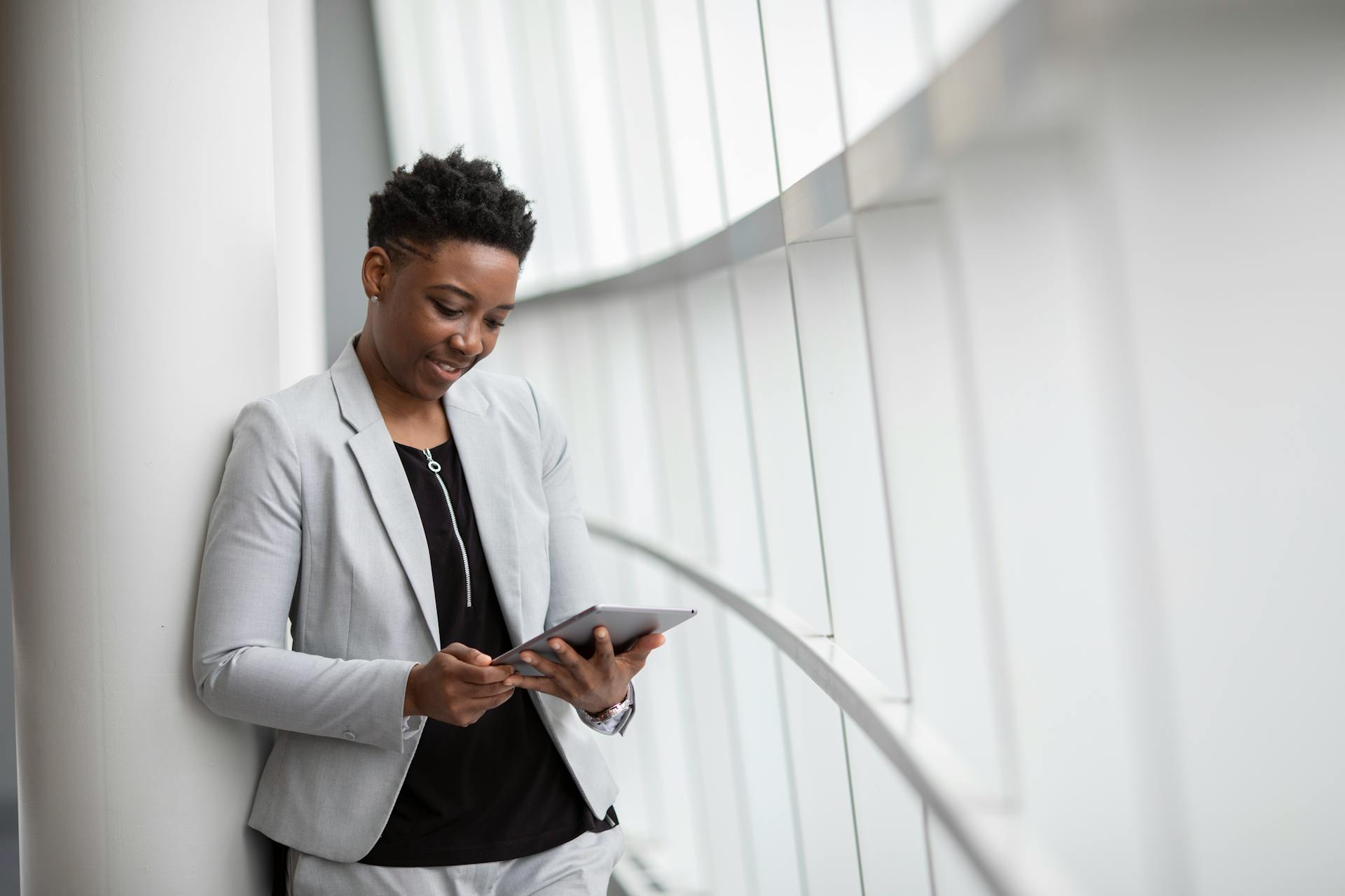 African American woman in business attire using a tablet in a bright, modern office setting.