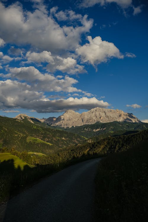 A road leading to a mountain range with clouds