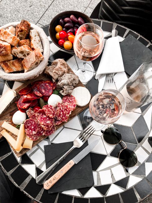 A gourmet charcuterie board with cheeses, meats, bread, and wine on a stylish mosaic table.