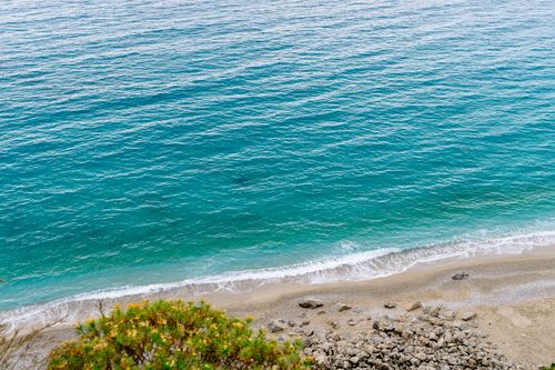 Free A breathtaking aerial view of a serene beach with turquoise waters, rocky shore, and gentle waves. Stock Photo