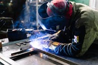 焊工在室内加工金属，火花明亮，烟雾升腾