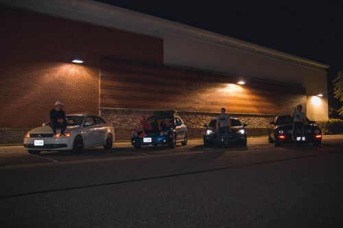 Free A group of friends sitting on cars in a dimly lit parking lot, enjoying a night out. Stock Photo