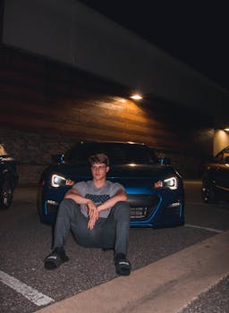 在弗吉尼亚州威廉斯堡，一个年轻人晚上坐在一辆蓝色跑车前，路灯照亮着周围
