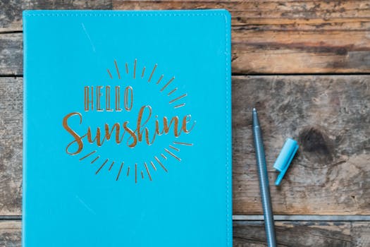 An uplifting 'Hello Sunshine' notebook on a rustic wooden table with a pen.