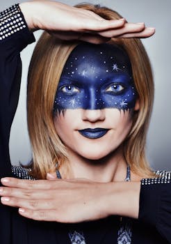 Portrait of a young woman with starry face paint framed by her hands, showcasing creative fashion and makeup.