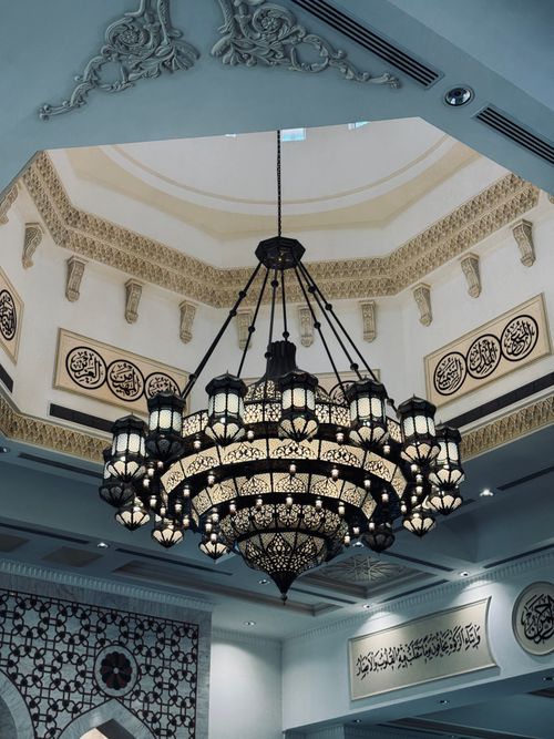 Free Intricate chandelier hanging in a beautifully decorated mosque interior with Arabic calligraphy. Stock Photo