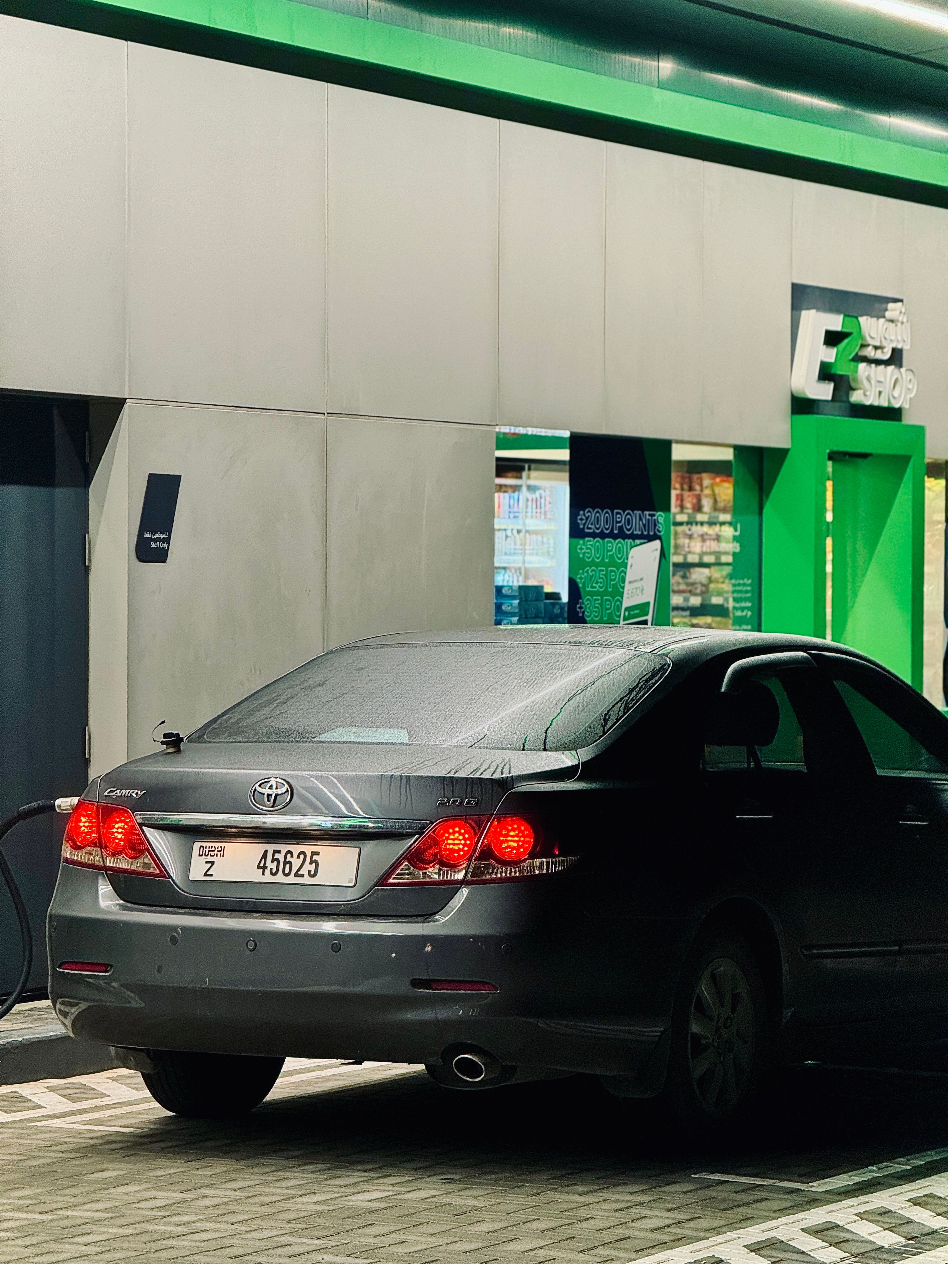 Dark sedan parked by a convenience store entrance at night, with a focus on vibrant green tones.