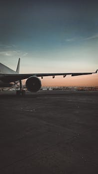 A large passenger airplane at an airport runway during sunset, showcasing the wing and engine.