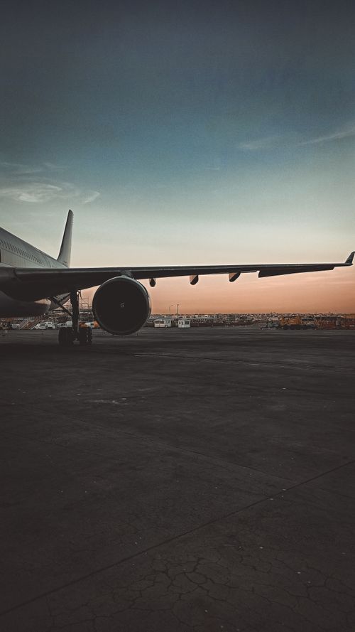 Free A large passenger airplane at an airport runway during sunset, showcasing the wing and engine. Stock Photo