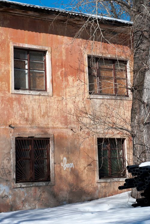 Free A weathered, abandoned apartment building with snow-covered ground and bare trees. Stock Photo