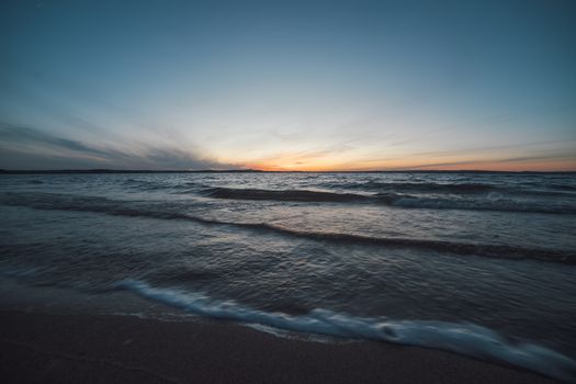 Peaceful sunrise on a beach with gentle waves and a clear horizon, captured in soft light.
