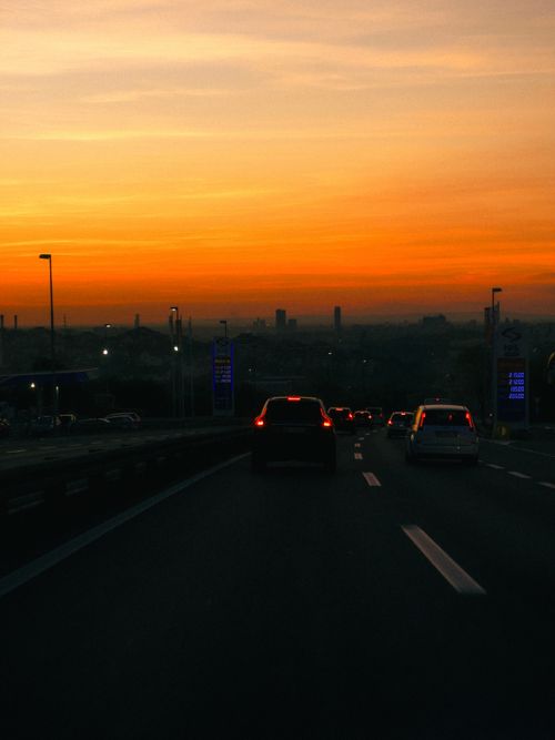 Free Cars driving on an urban highway at sunset, with a dramatic orange sky. Stock Photo