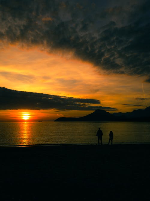 Two people are standing on the beach at sunset