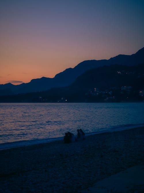Two people sitting on the beach at sunset